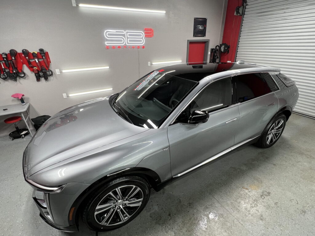 Sleek silver SUV with a glossy finish parked inside a detailing garage, with SB3 Coatings branding on the wall and detailing tools neatly arranged nearby.