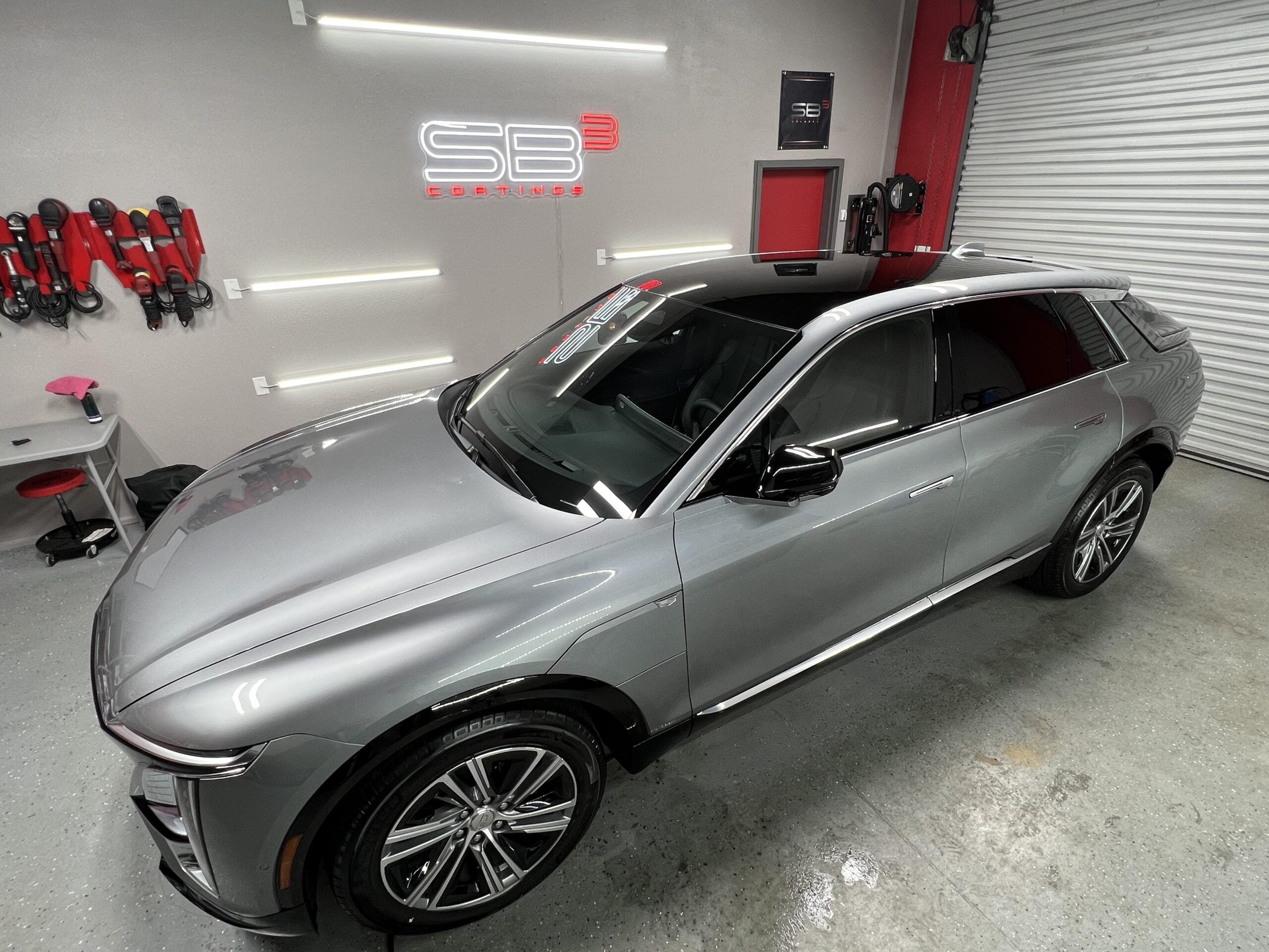 Sleek silver SUV with a glossy finish parked inside a detailing garage, with SB3 Coatings branding on the wall and detailing tools neatly arranged nearby.