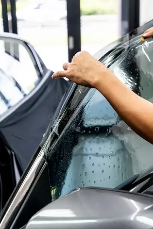 Close-up of a technician applying window tint film to a car door window, with water bubbles visible between the glass and the film.
