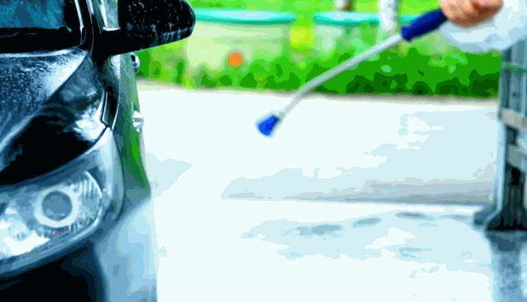 Car being pressure washed before ceramic coating, with water spraying over the black front end near the headlight.