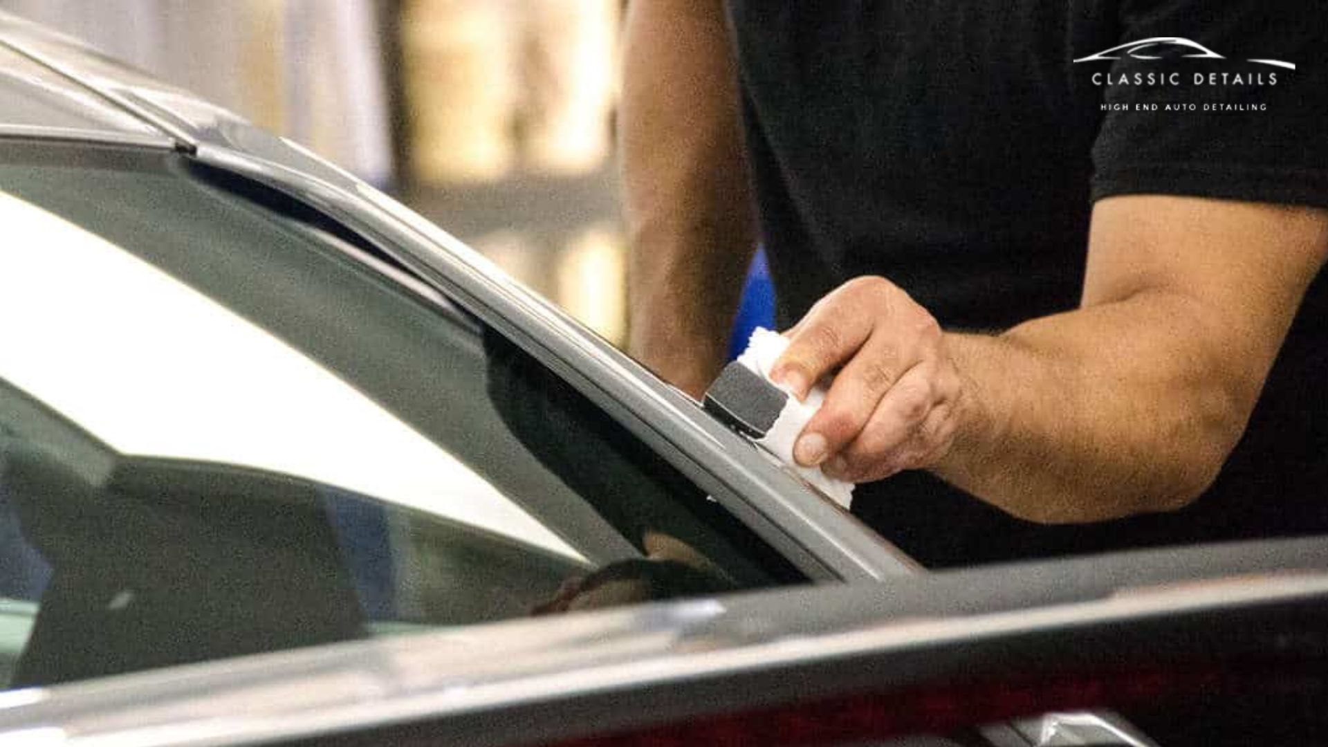 Detailer applying ceramic coating along the edge of a car window trim using an applicator pad and microfiber cloth.