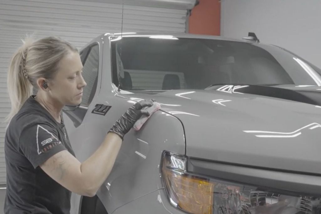 Detailing technician performing professional ceramic coating application on a white pickup truck inside an auto detailing studio.