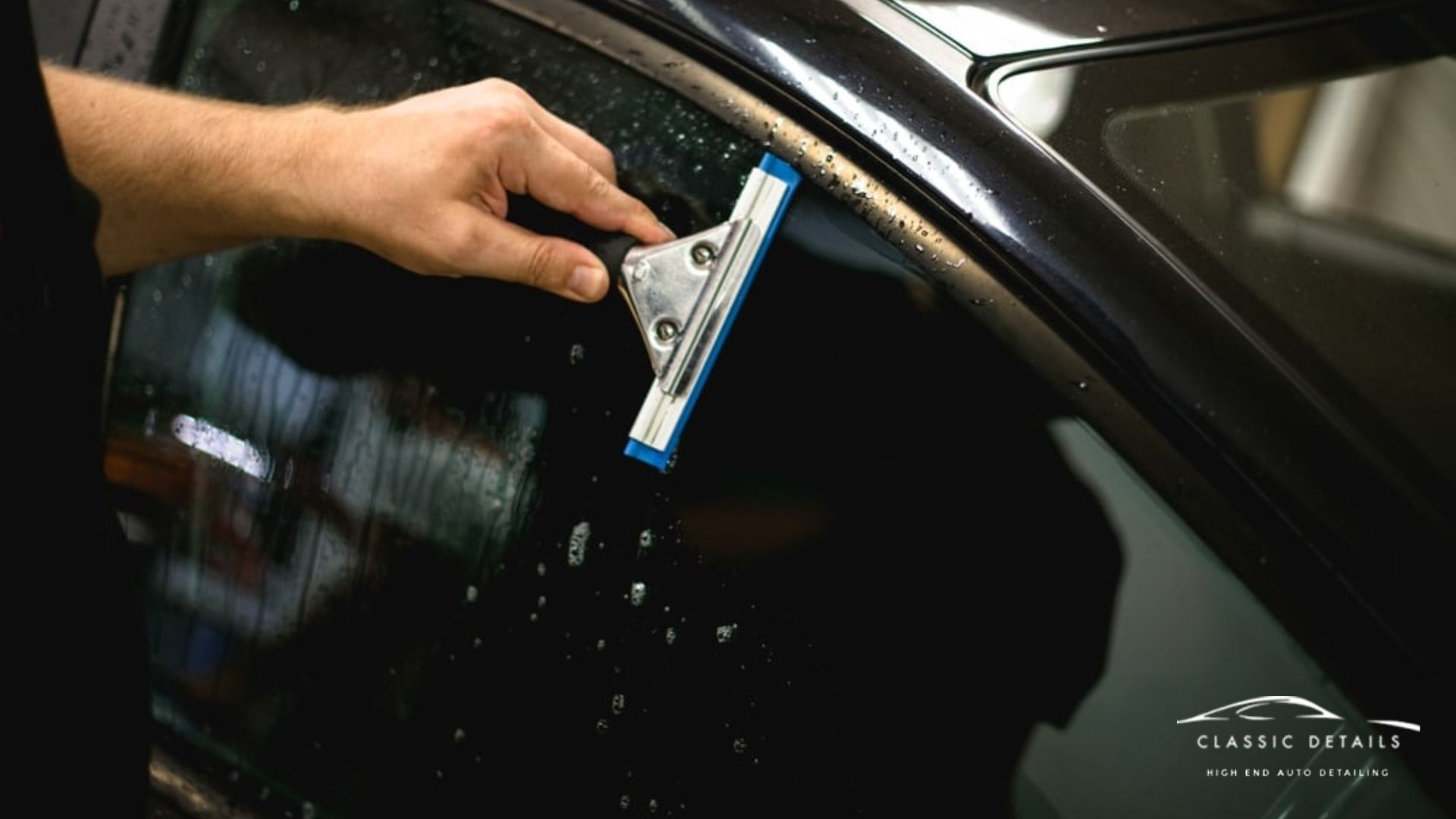 Technician using a squeegee to smooth Window Tint film onto a car side window. Water droplets on the glass show the installation process in progress for a clean bubble free finish.