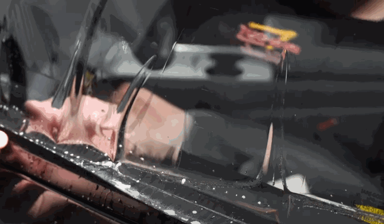 Close up of window tint film being carefully positioned along the edge of a car window with water droplets visible during installation. The flexible film is adjusted to fit perfectly for a clean window tint result.