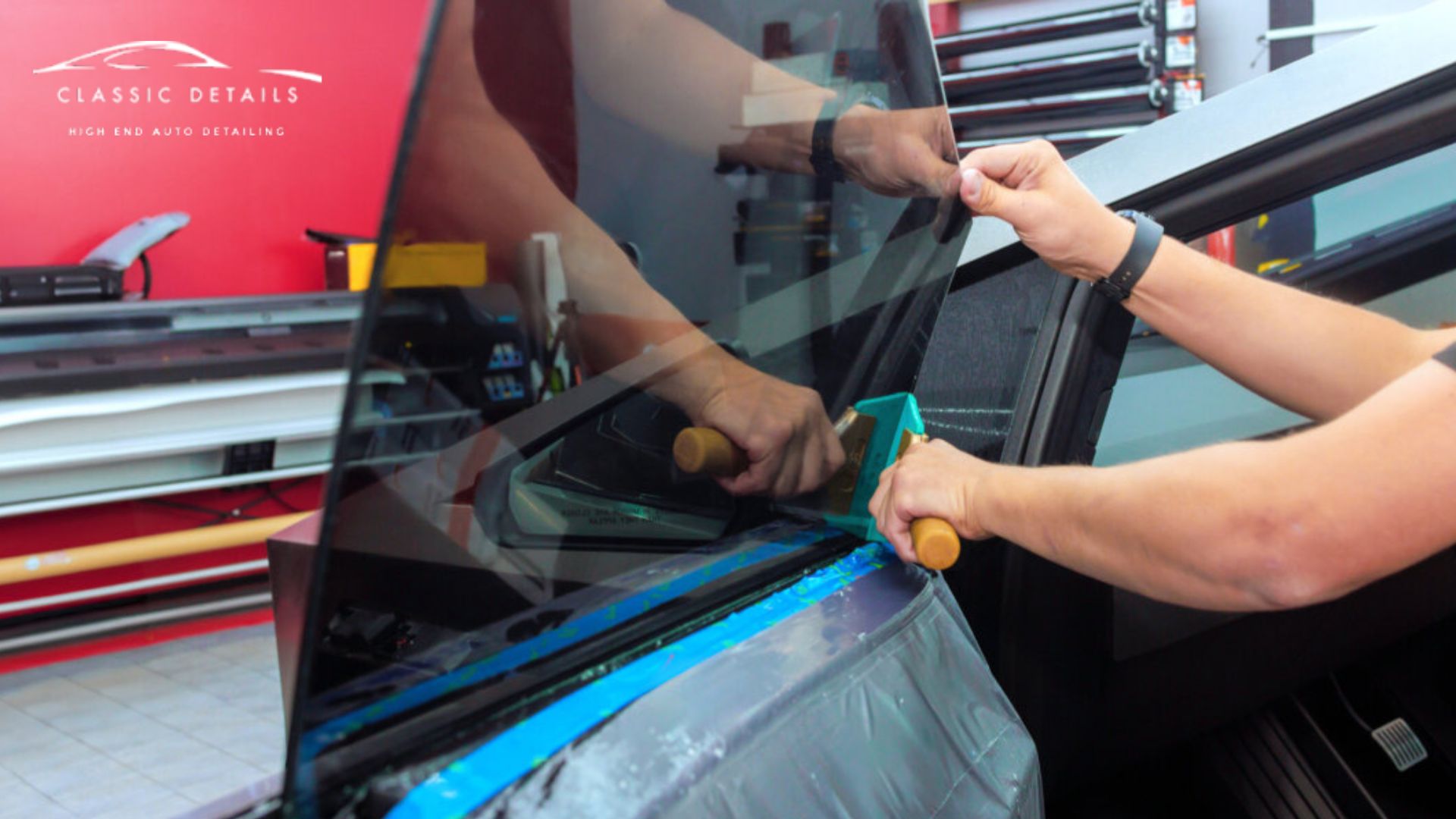 Technician uses a squeegee tool to smooth window tint film onto a car door window while holding the film in place.