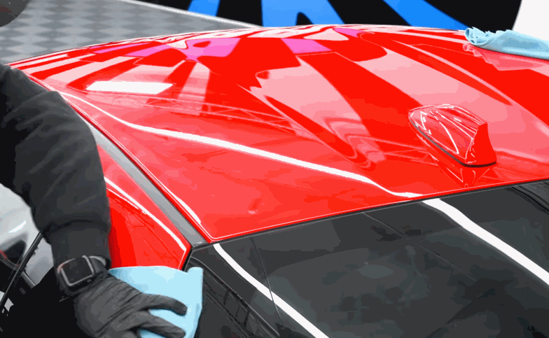 A technician wipes a red car roof with a microfiber towel after protective coating has been applied.