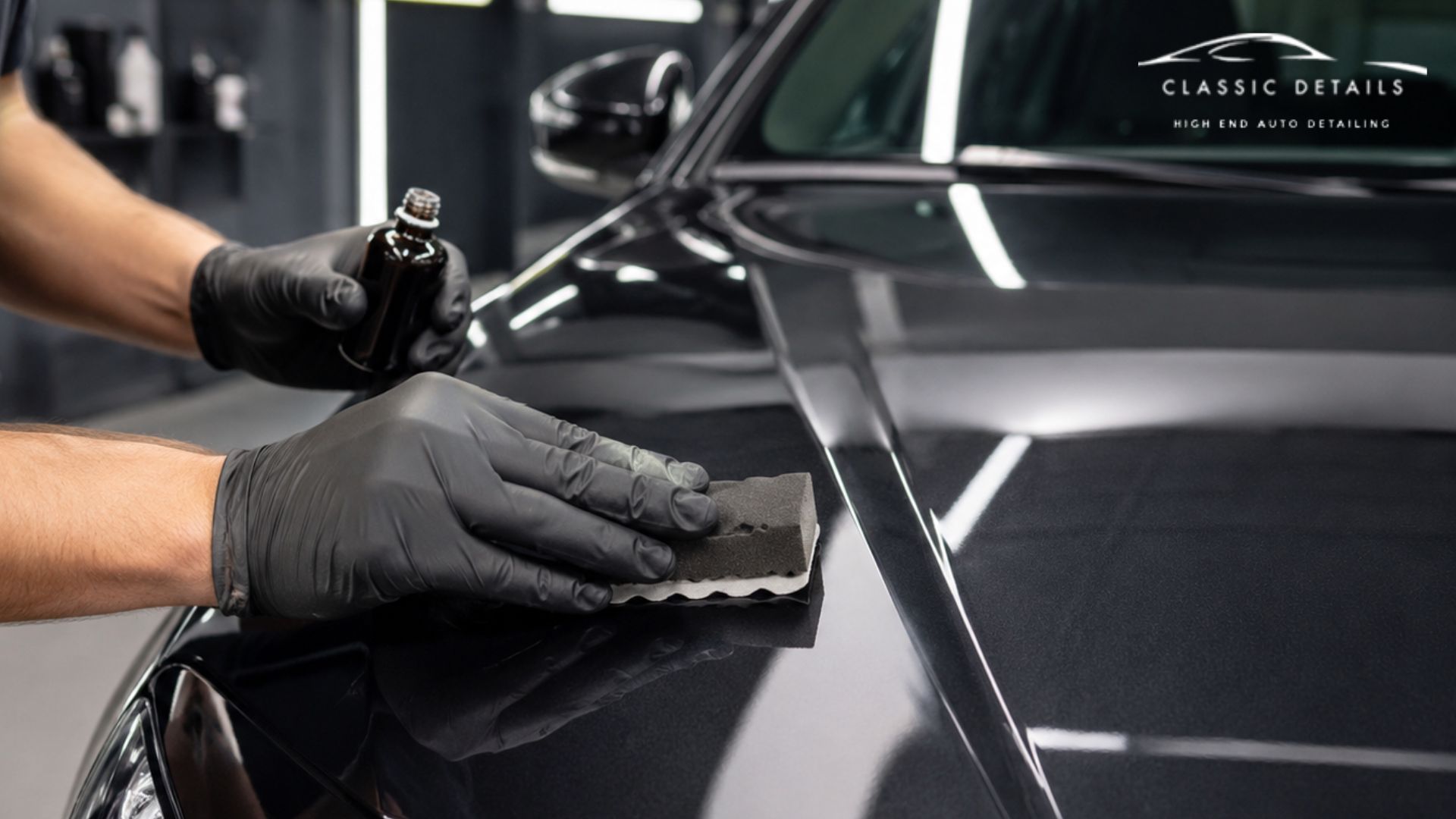 A technician applies ceramic coating to a black vehicle hood with an applicator pad.