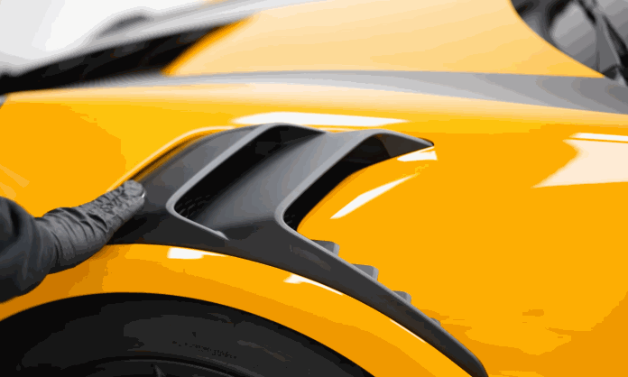 Gloved hand checks the glossy black trim and yellow fender of a freshly detailed car.