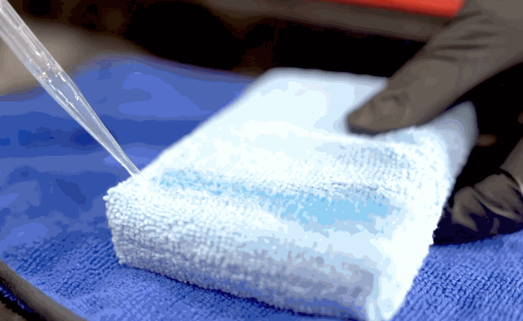 Ceramic coating liquid is poured onto a microfiber applicator towel before application.