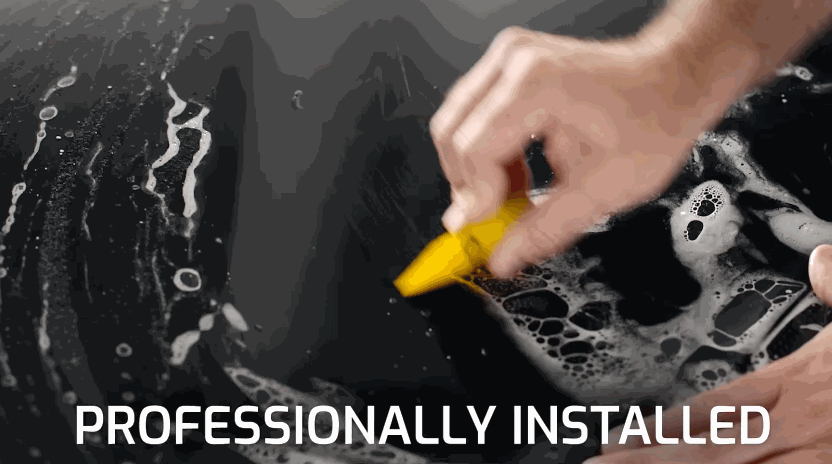 Close-up of a technician using a yellow squeegee to smooth paint protection film onto a black vehicle surface during a professional installation.
